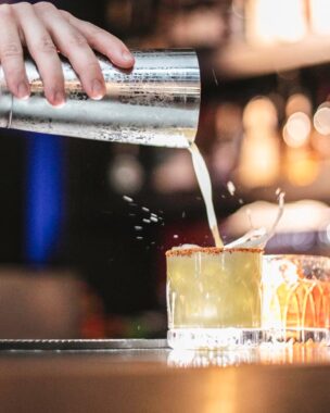 person pouring a cocktail into a glass